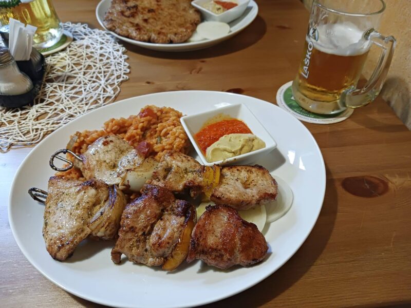 A dish of food with rice and meat, with a glass of beer in the background